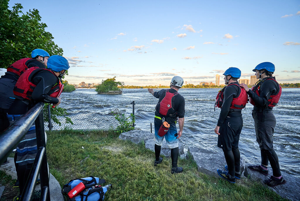 A whitewater instructor showing students where to paddle from the shore of Kichi Sibi (Ottawa River).
